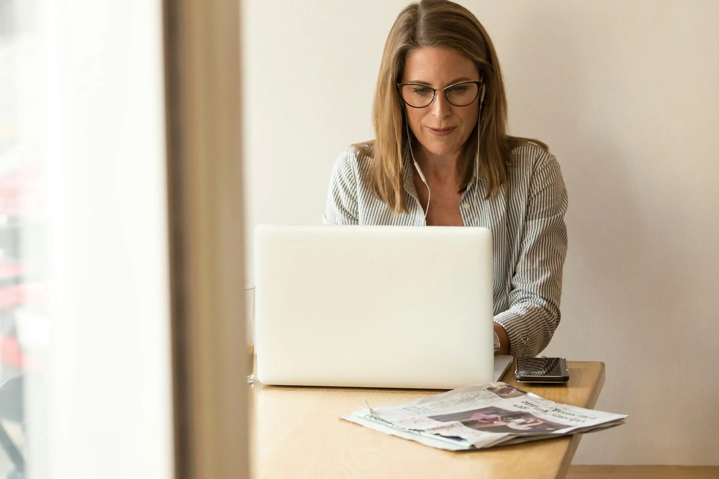 Adviseur met bril werkt geconcentreerd op een laptop aan een lichte houten tafel bij het raam