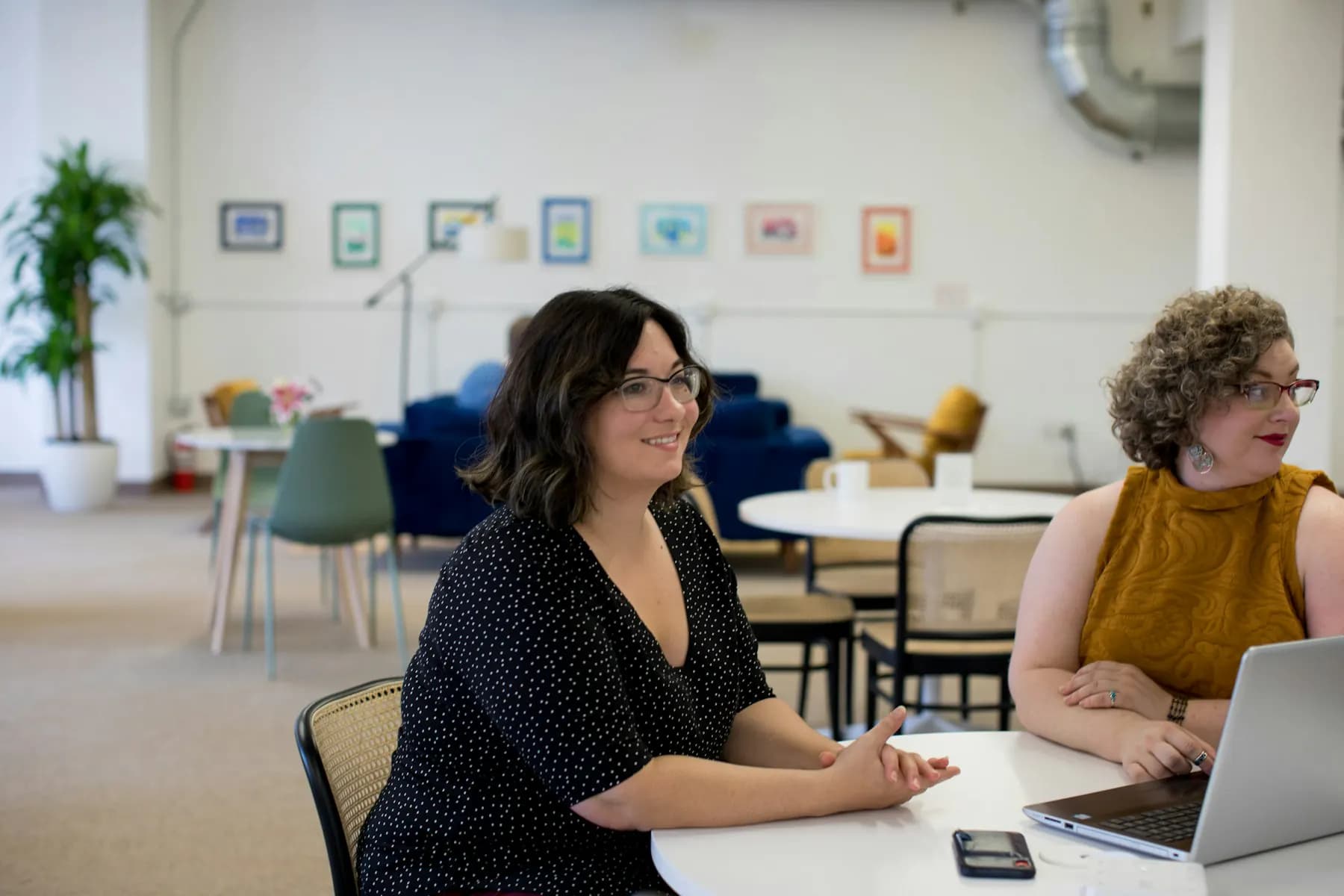 Twee collega's in gesprek aan een ronde tafel met laptop in een licht, open kantoor